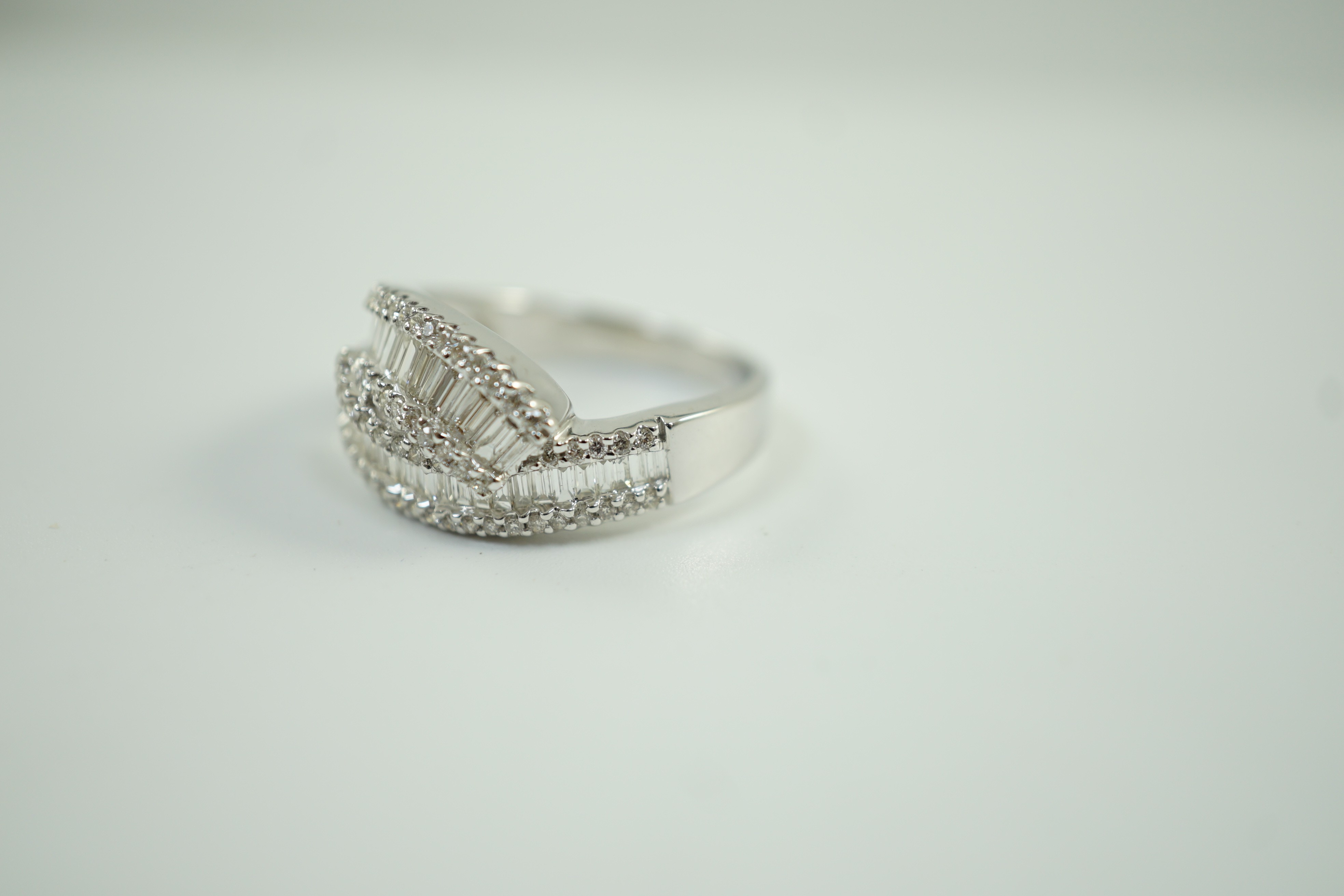 A modern 18ct white gold, baguette cut and diamond chip cluster set crossover ring, size O, gross weight 4.7 grams.
